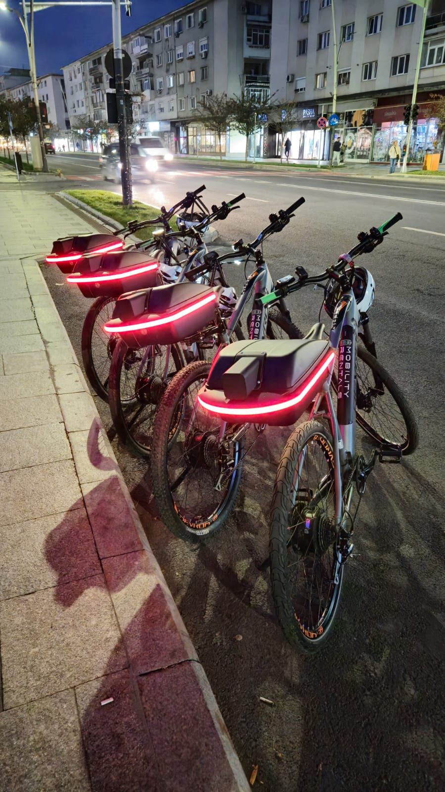 Four bikes parked on pavement with red glowing strip light at rear