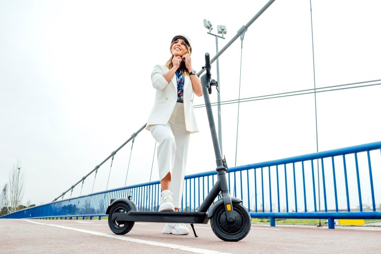 A woman putting on a helmet to use a folding electric scooter