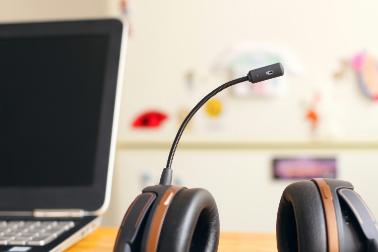 Headset with microphone next to a laptop on a desk in a bright room.