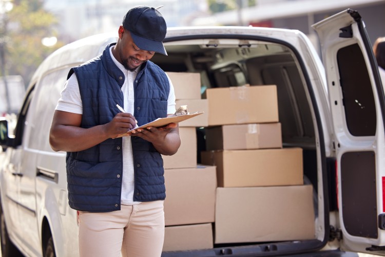 Man writing on clipboard stands in front of van filled with parcels