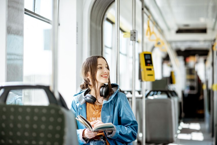 Woman sitting on bus wearing blue jacket and headphones, smiling