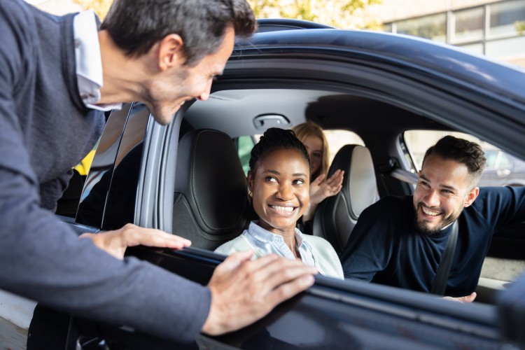 two people in a car, smiling at a man leaning down towards the front passenger window