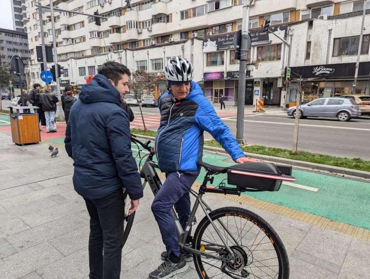 man in blue jacket using bike, talking to another man at the side of the road