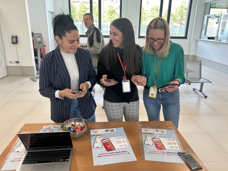 Three women holding phones and smiling stand behind a desk