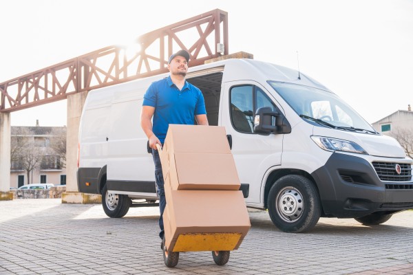 Delivery driver transporting packages with hand truck in front of van.