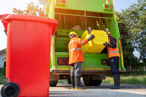 Two sanitary workers loading garbage into waste truck