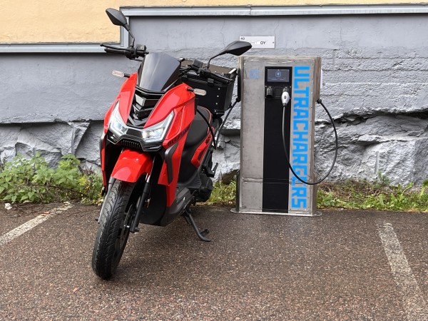 Electric moped plugged into an UltraChargers charging station outdoors.