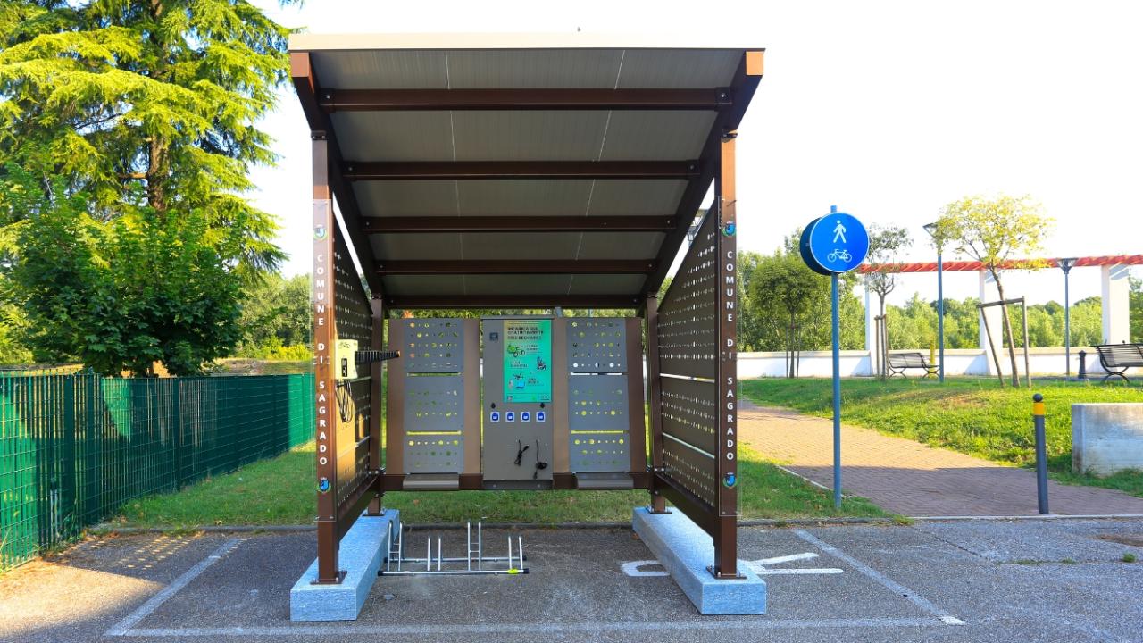 A solar-powered shelter in a green urban park with dedicated bike racks and perforated side panels.