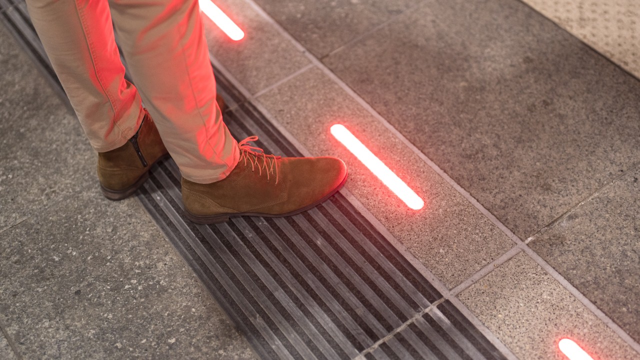 Person standing near a red illuminated platform edge indicating a danger zone before a train arrival.