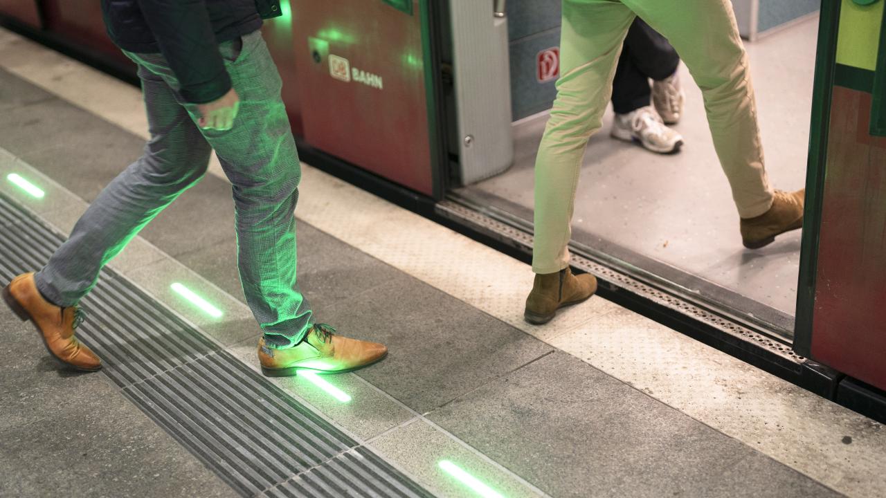 Close-up of green illuminated platform edge lighting at a train station, showing passengers boarding safely.