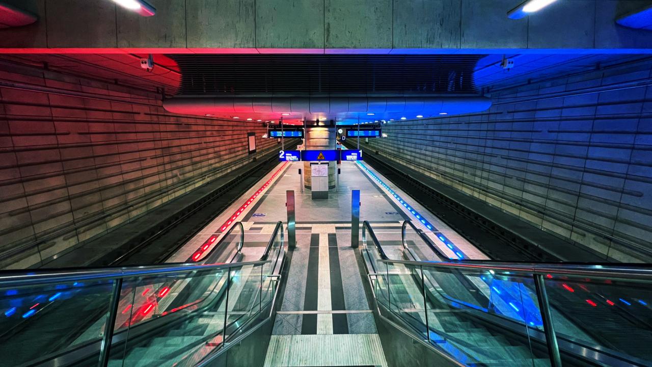 Escalator area in a modern underground station with blue and red lighting effects illustrating intelligent illumination technology.